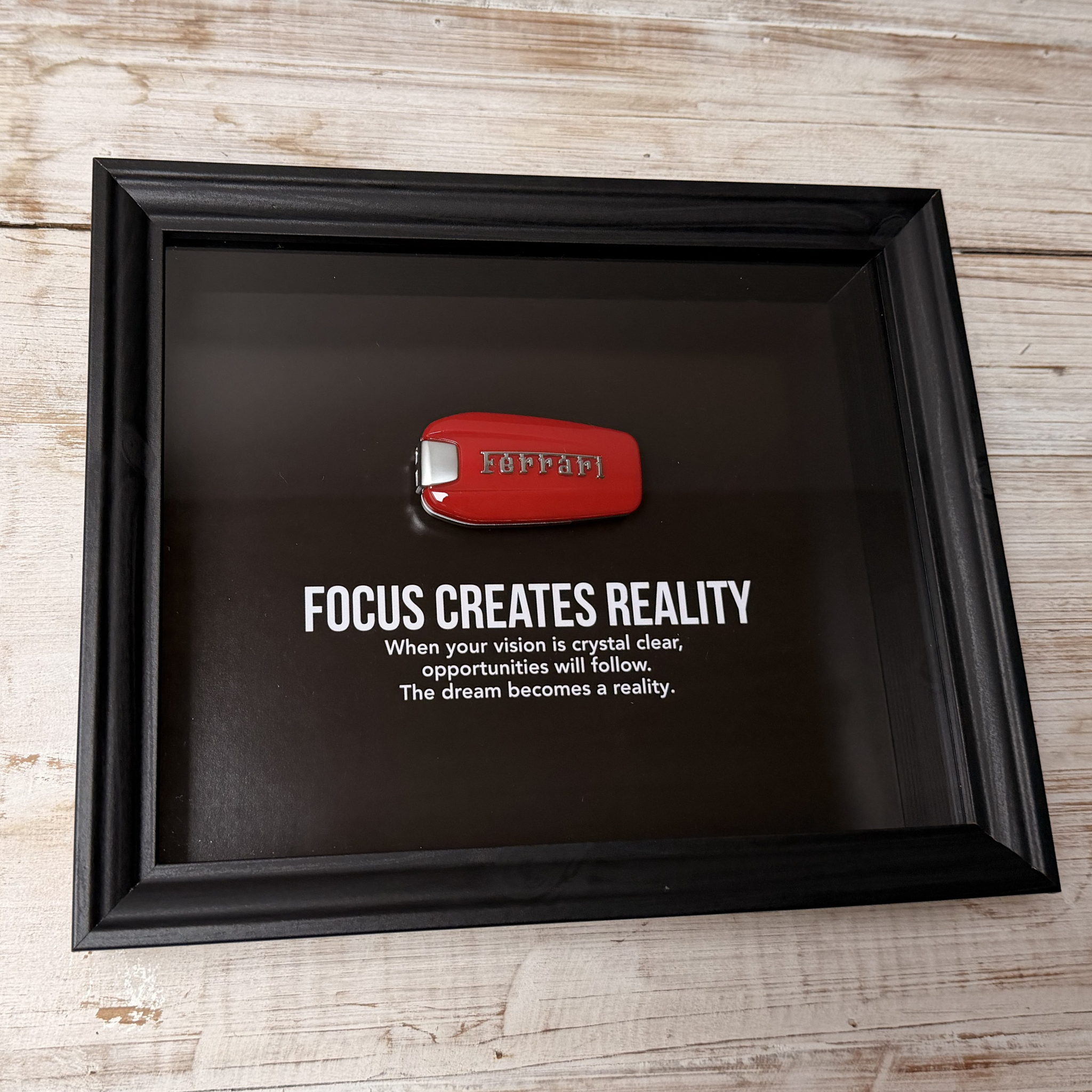 Een zwart stijlvol foto-frame met daarin een echte Ferrari autosleutel. in het frame zien we een motivatie tekst om mensen te inspireren richting hun eigen droomwagen.