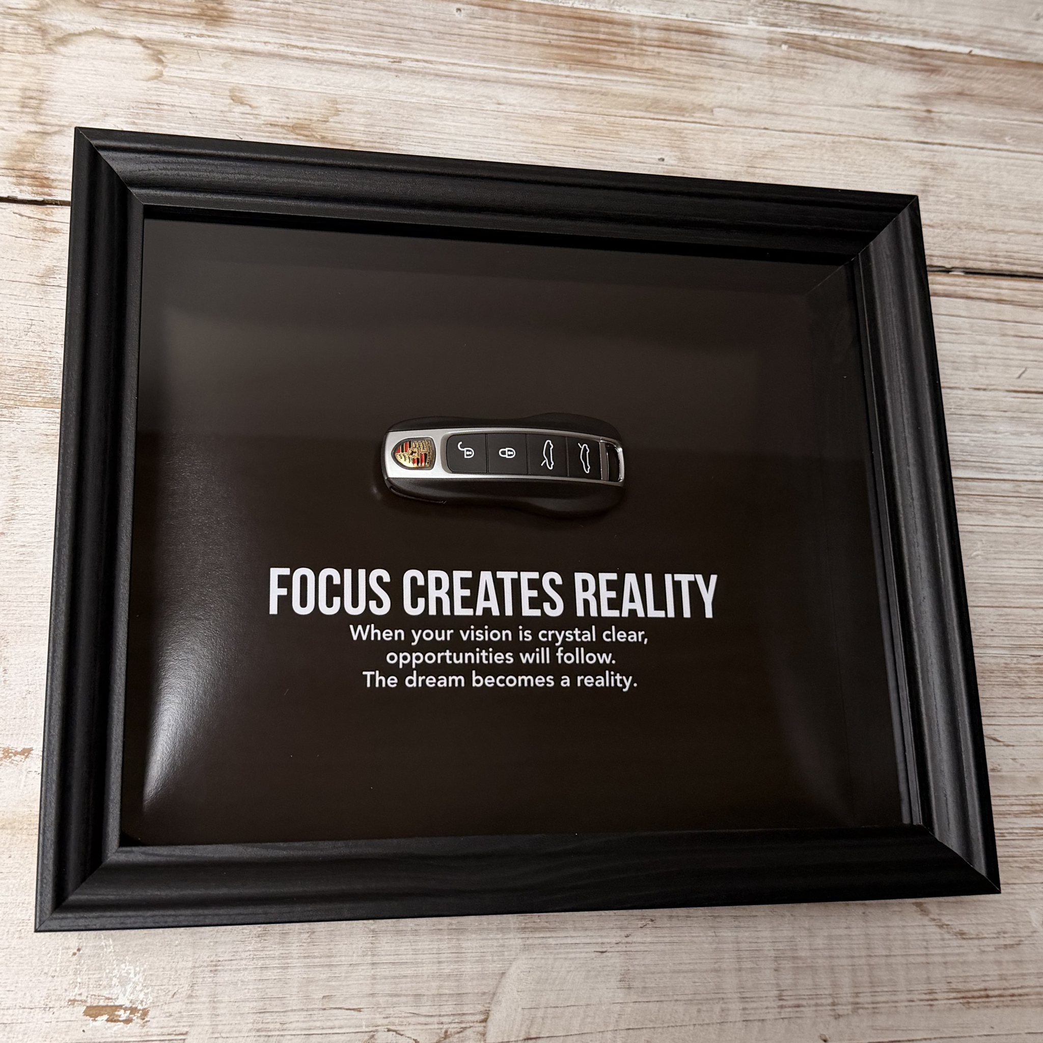Een zwart stijlvol foto-frame met daarin een echte porsche autosleutel. in het frame zien we een motivatie tekst om mensen te inspireren richting hun eigen droomwagen. 