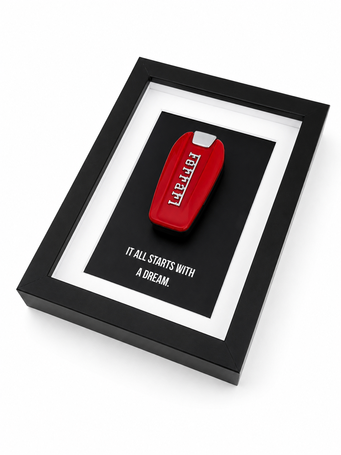 een zwart kader voor op een bureau of aan een muur met motiverende tekst: it all starts with a dream. In de kader hangt een echte rode ferrari sleutel. 