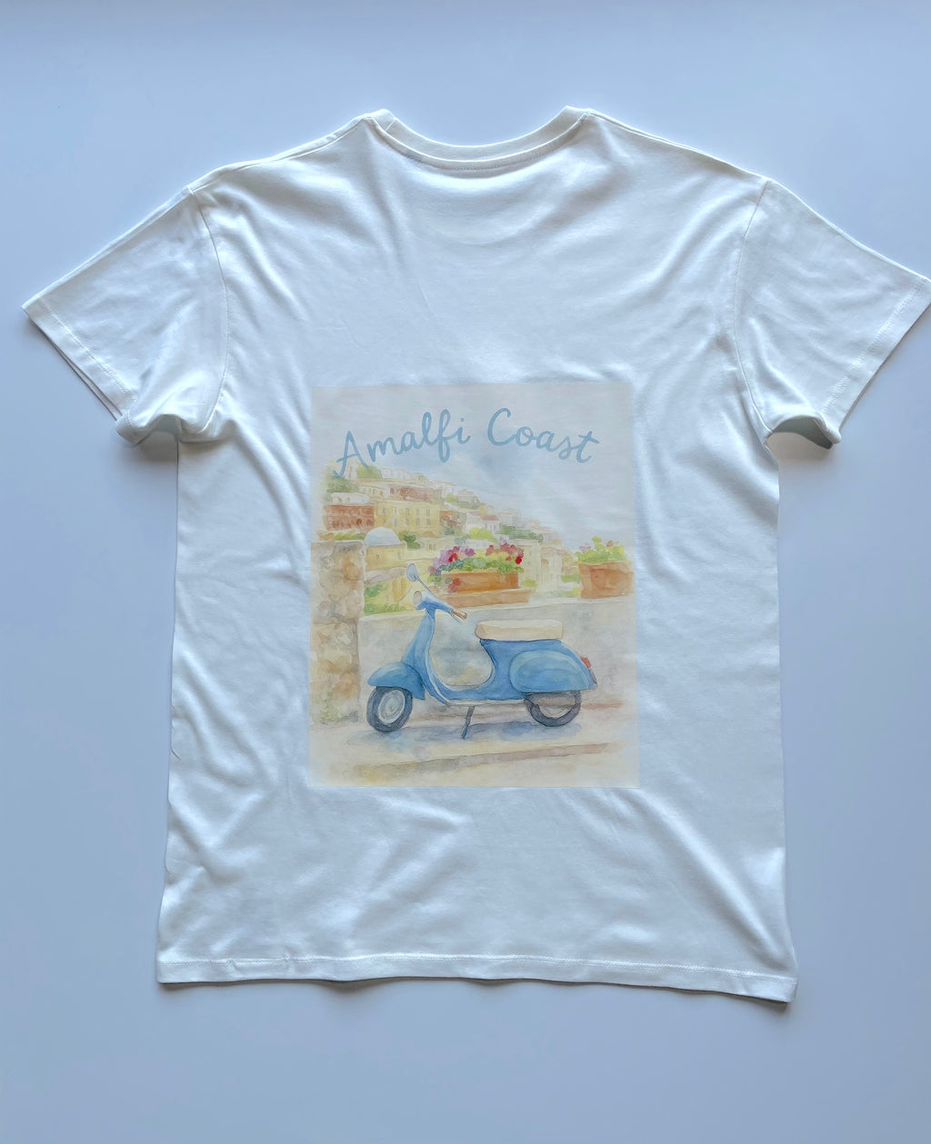 Een wit t-shirt met een kleurrijke aquarel ontwerp van een blauwe vespa met een italiaanse geinspireerde achtergrond. 