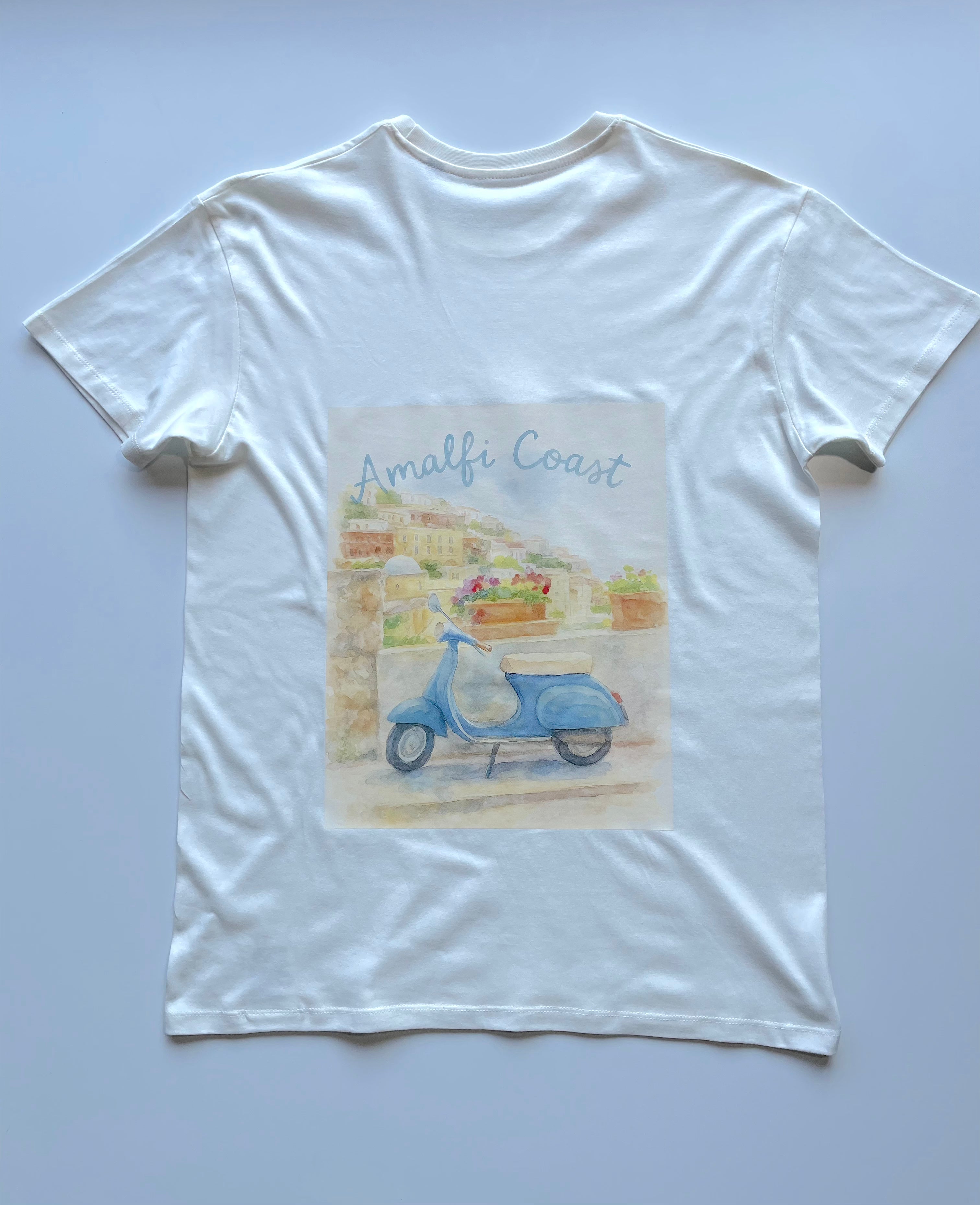 Een wit t-shirt met een kleurrijke aquarel ontwerp van een blauwe vespa met een italiaanse geinspireerde achtergrond. 