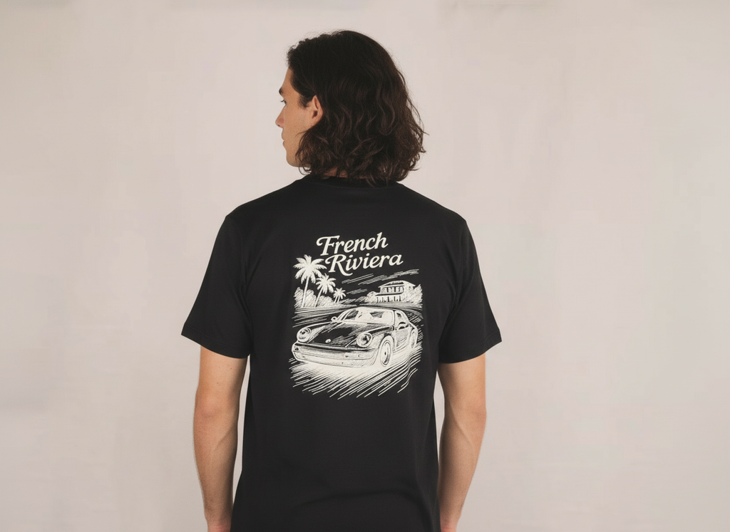 een jonge man draagt een zwart losse fit t-shirt met een French Riviera geïnspireerd ontwerp. met een Porsche afgebeeld. klassieke motorsport, autosport en auto's. automotive.  verkrijgbaar in small, medium en large. premium kwaliteit.