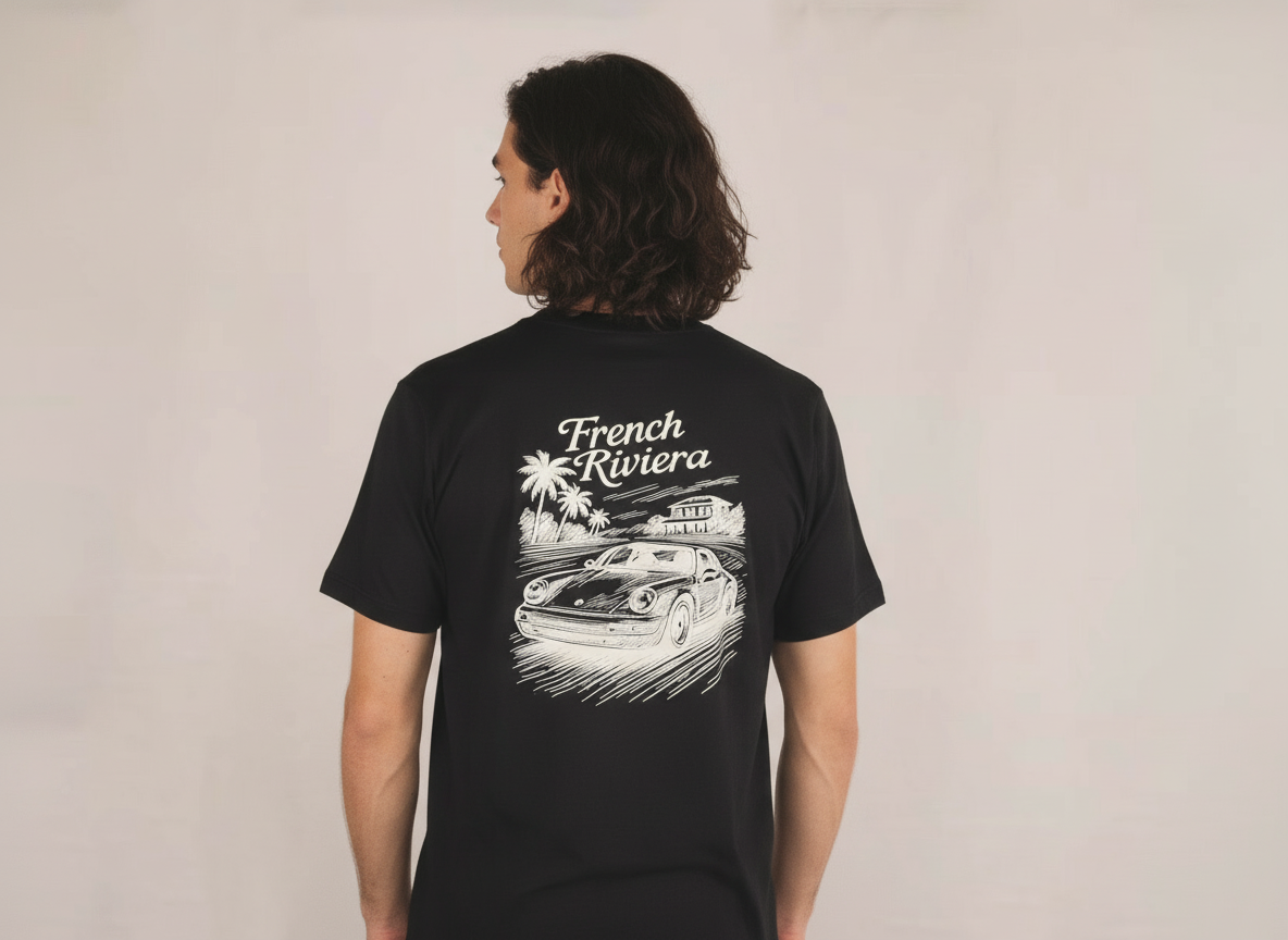 een jonge man draagt een zwart losse fit t-shirt met een French Riviera geïnspireerd ontwerp. met een Porsche afgebeeld. klassieke motorsport, autosport en auto's. automotive.  verkrijgbaar in small, medium en large. premium kwaliteit.