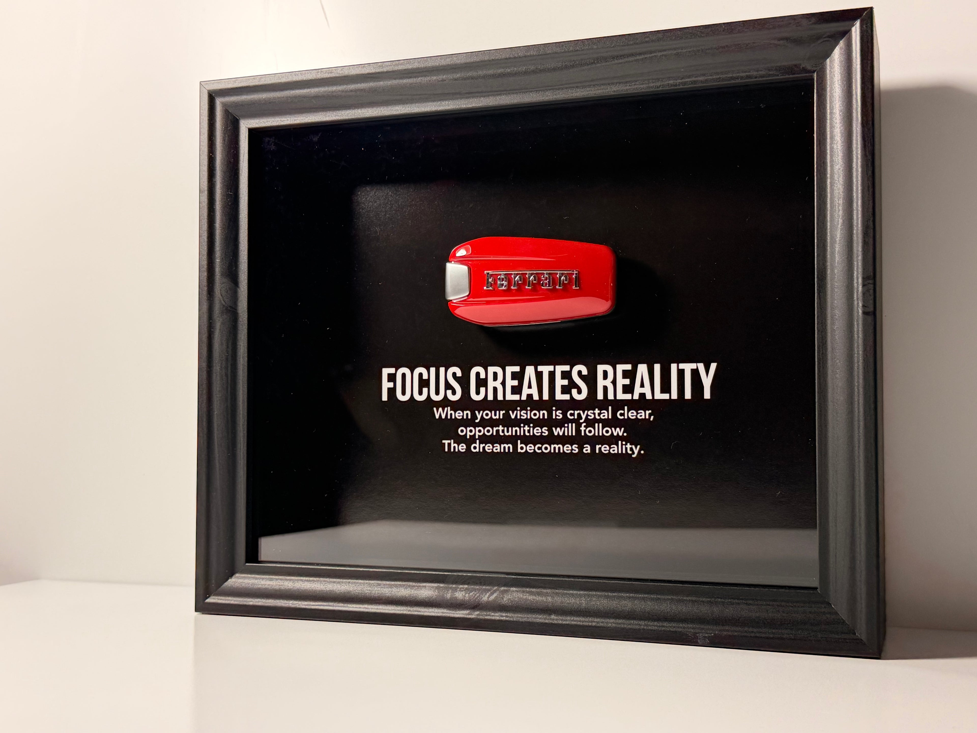 een stijlvolle zwarte kader, met een zwarte achtergrond, met een echte Ferrari sleutel. de motiverende tekst in het kader leest: Focus creates reality. 