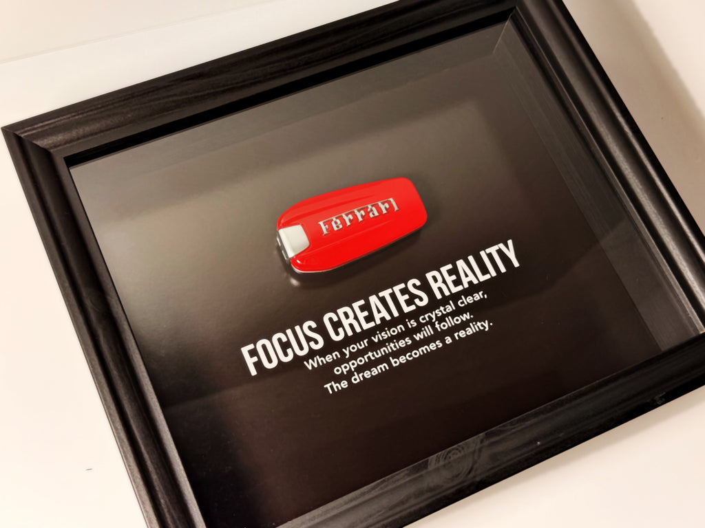 een stijlvolle zwarte kader, met een zwarte achtergrond, met een echte Ferrari sleutel. de motiverende tekst in het kader leest: Focus creates reality. 