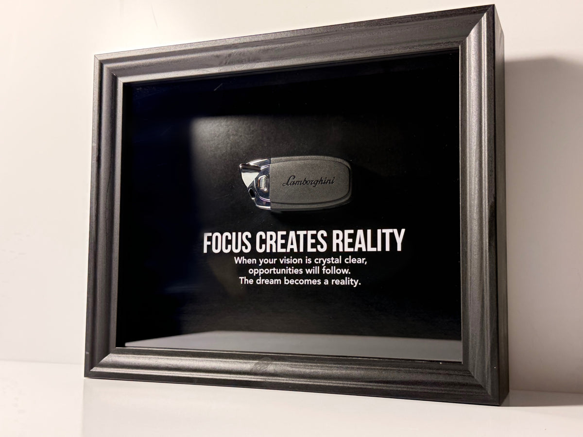 een stijlvolle zwarte kader, met een zwarte achtergrond, met een echte Lamborghini sleutel. de motiverende tekst in het kader leest: Focus creates reality. 