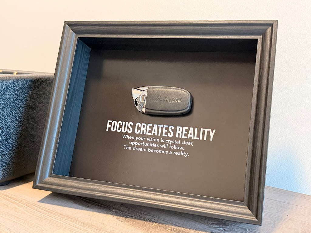 Een zwart stijlvol foto-frame met daarin een echte Lamborghini autosleutel. in het frame zien we een motivatie tekst om mensen te inspireren richting hun eigen droomwagen. 