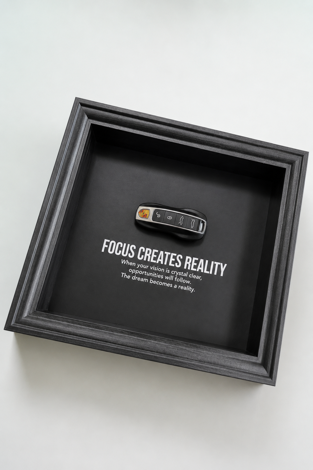 Een zwart stijlvol foto-frame met daarin een echte porsche autosleutel. in het frame zien we een motivatie tekst om mensen te inspireren richting hun eigen droomwagen.
