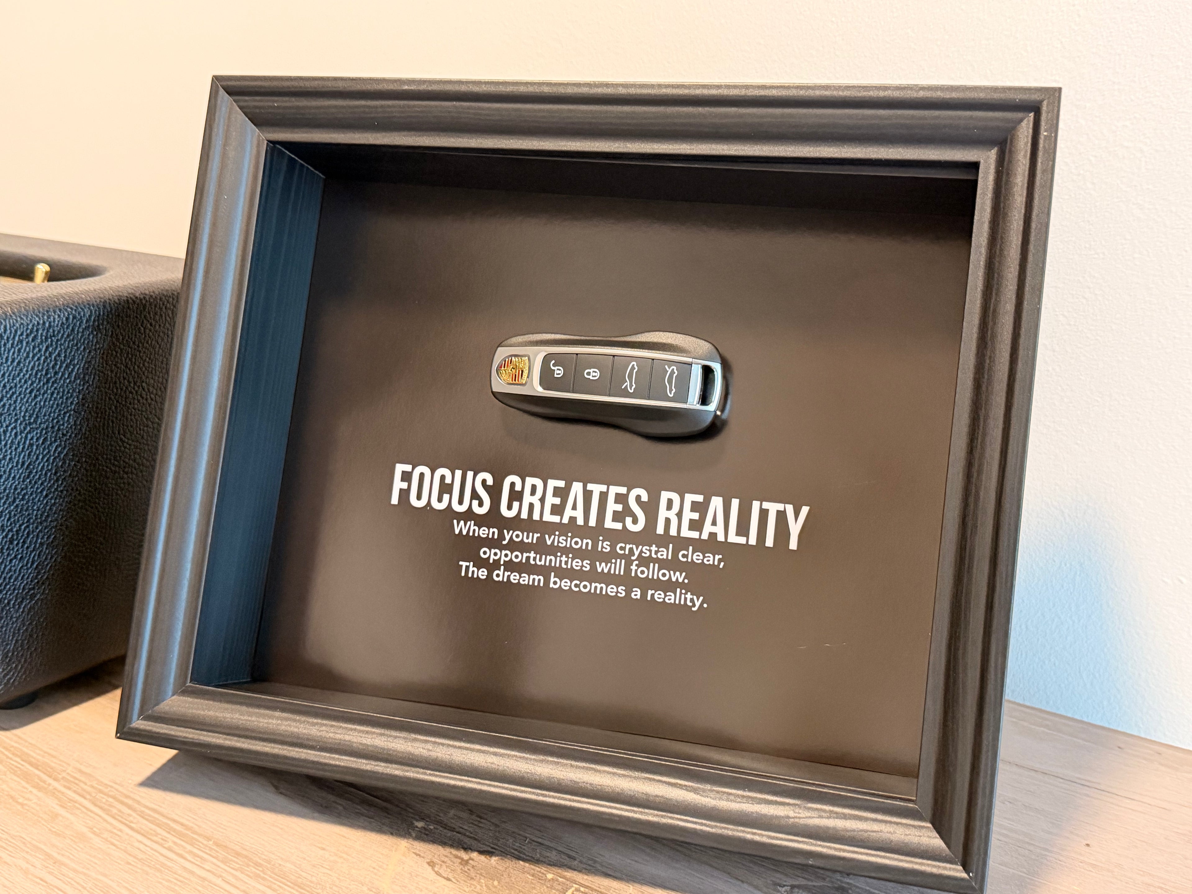 Een zwart stijlvol foto-frame met daarin een echte porsche autosleutel. in het frame zien we een motivatie tekst om mensen te inspireren richting hun eigen droomwagen. 