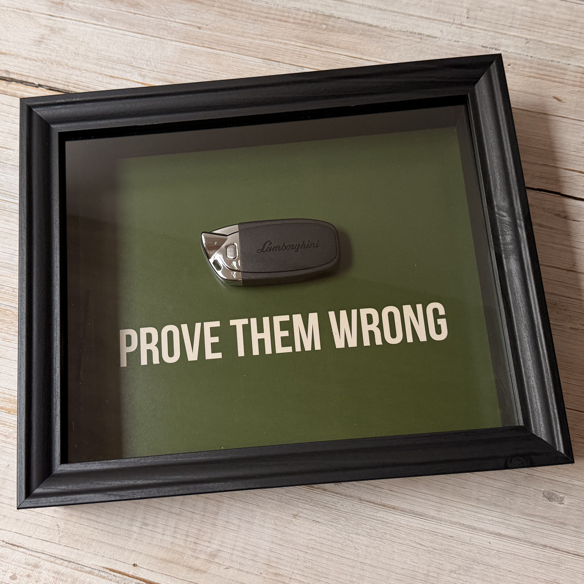 Een zwart stijlvol foto-frame met daarin een echte Lamborghini autosleutel. in het frame zien we een motivatie tekst om mensen te inspireren richting hun eigen droomwagen. De tekst: Prove them wrong. 